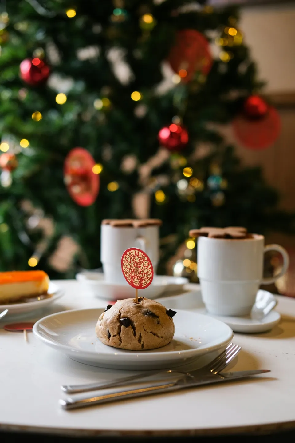A chocolate chunk cookie with two hot chocolates behind