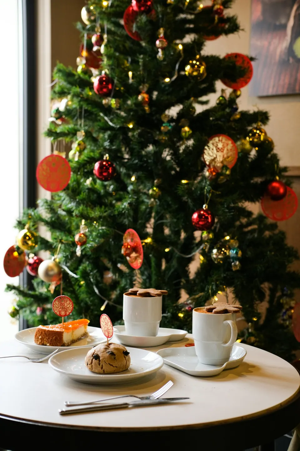 The table set with hot chocolates, cheesecake and a cookie by the tree