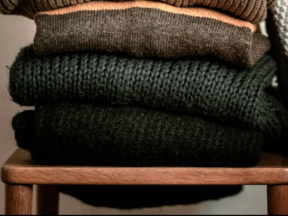 Folded brown and dark green knitted jumpers on a wooden stool